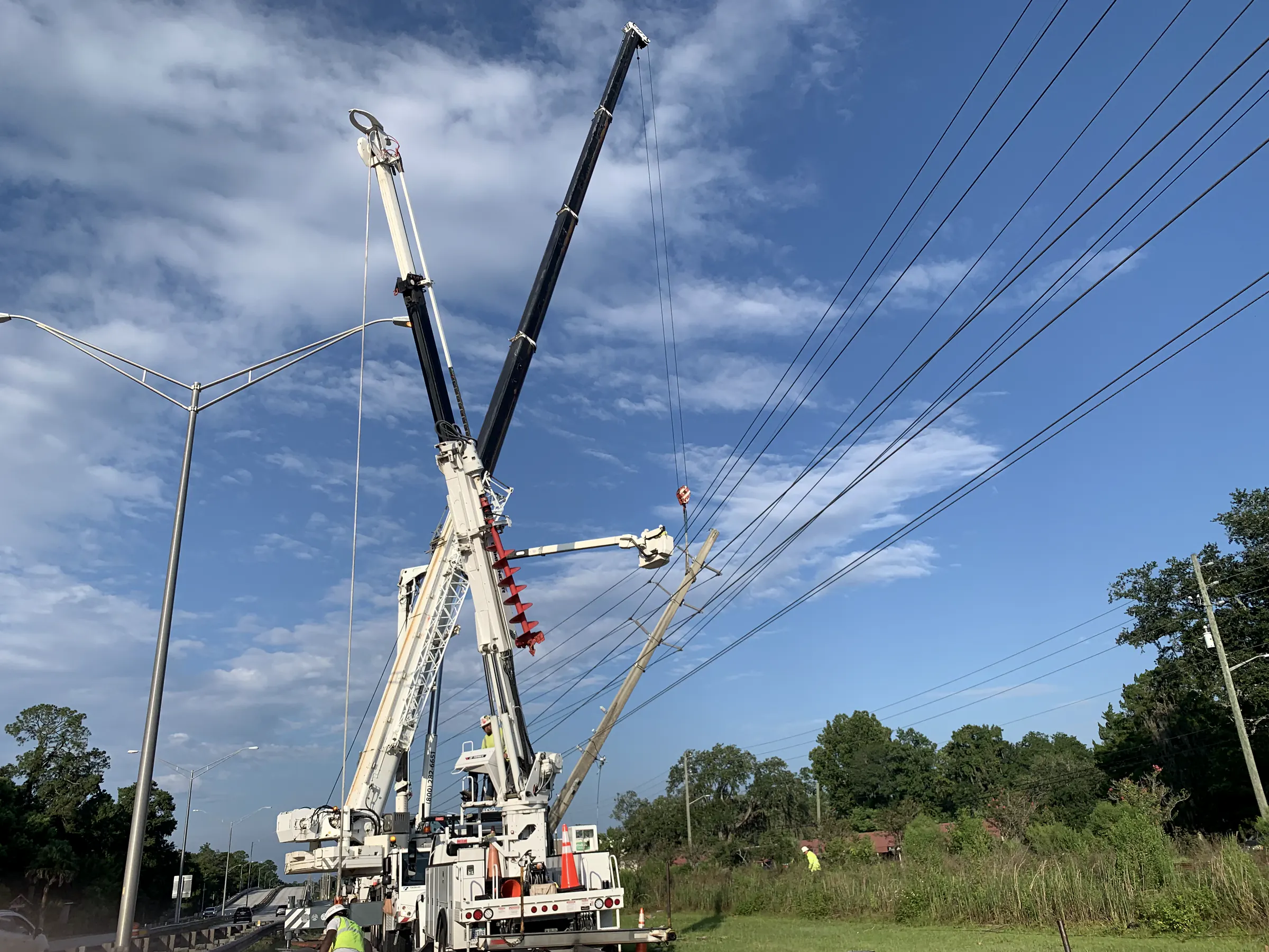 Bucket trucks and a crane working on overhead utility lines beside a roadway