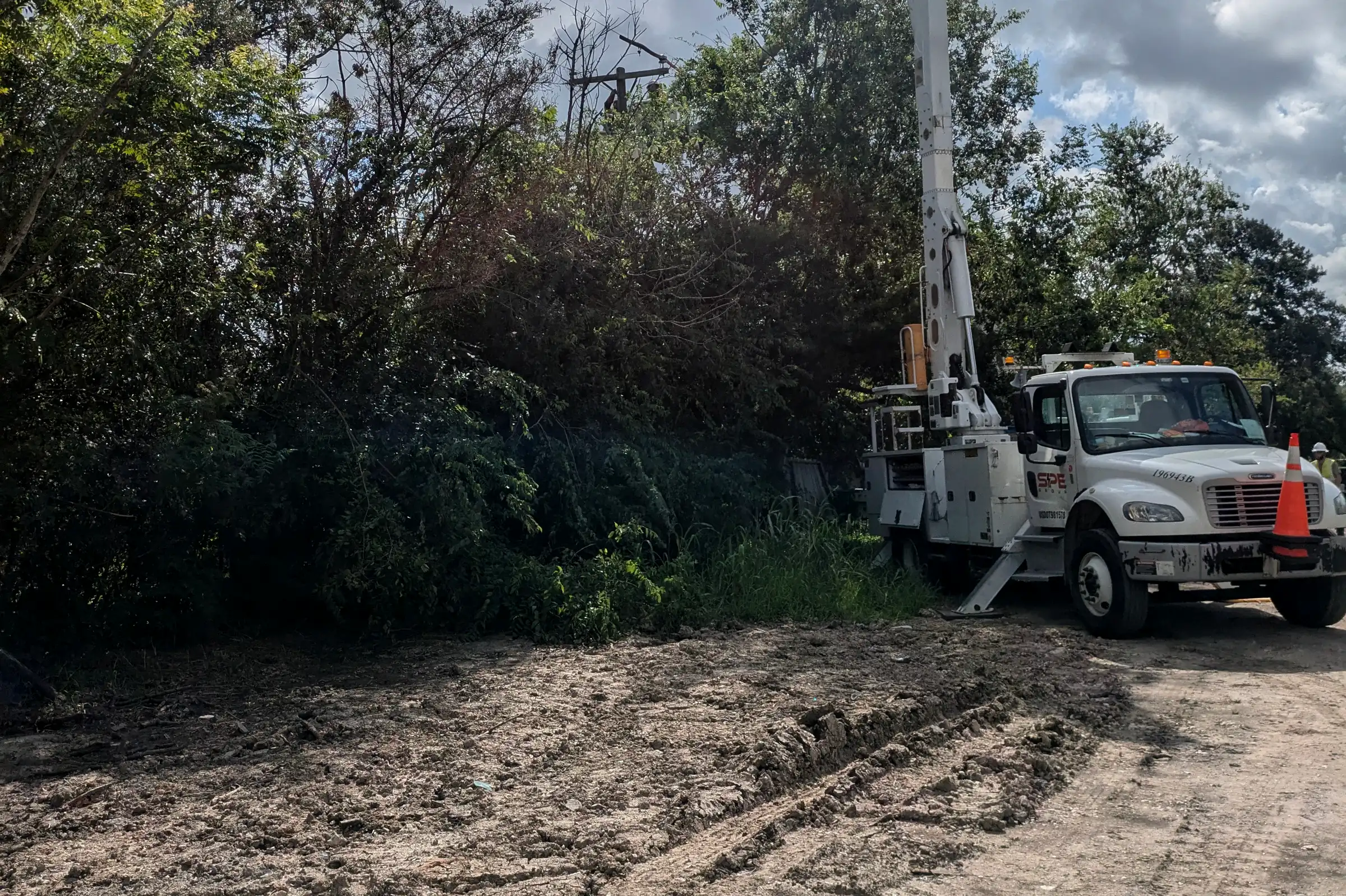 SPE bucket truck with its boom raised into storm-damaged trees beside a dirt track