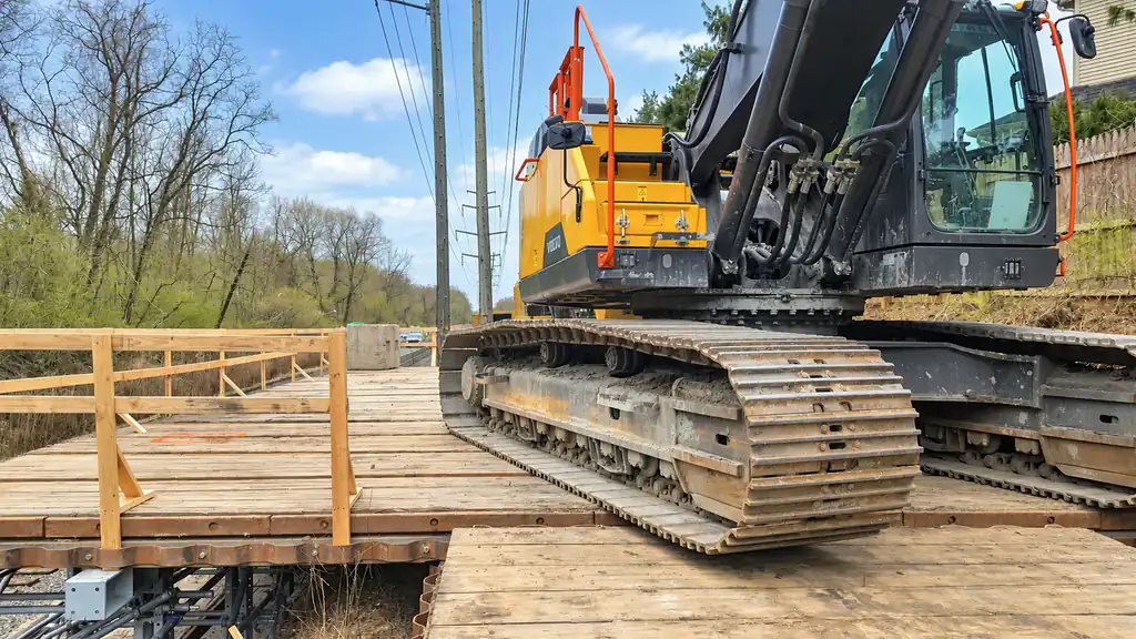 Excavator standing on timber access mats beside utility lines
