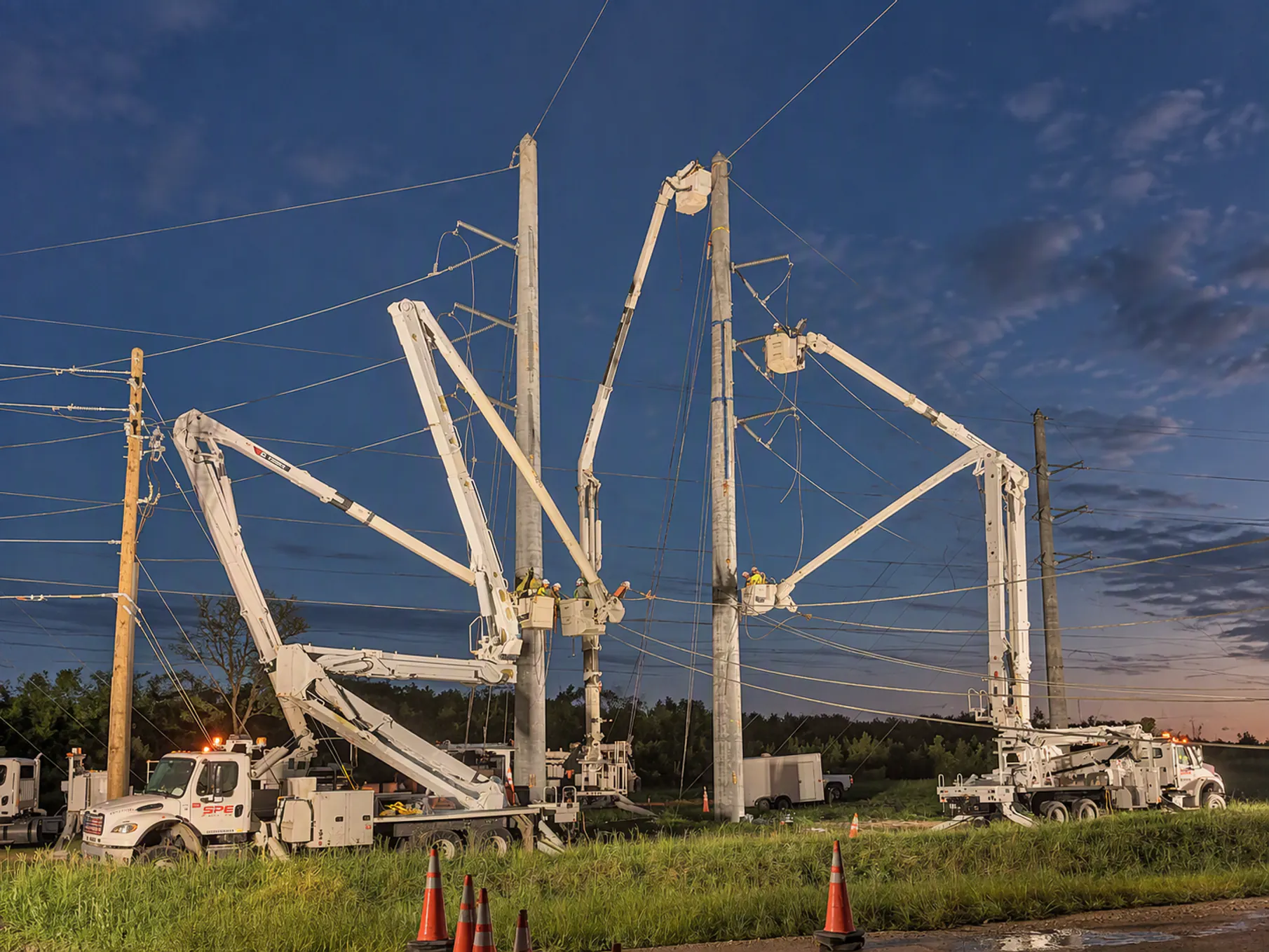 SPE bucket trucks working two transmission poles at dusk